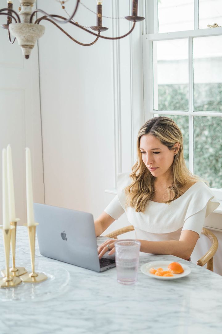 Tamara Ashworth working on a laptop at a marble table beside a window, with candlesticks in the foreground.
